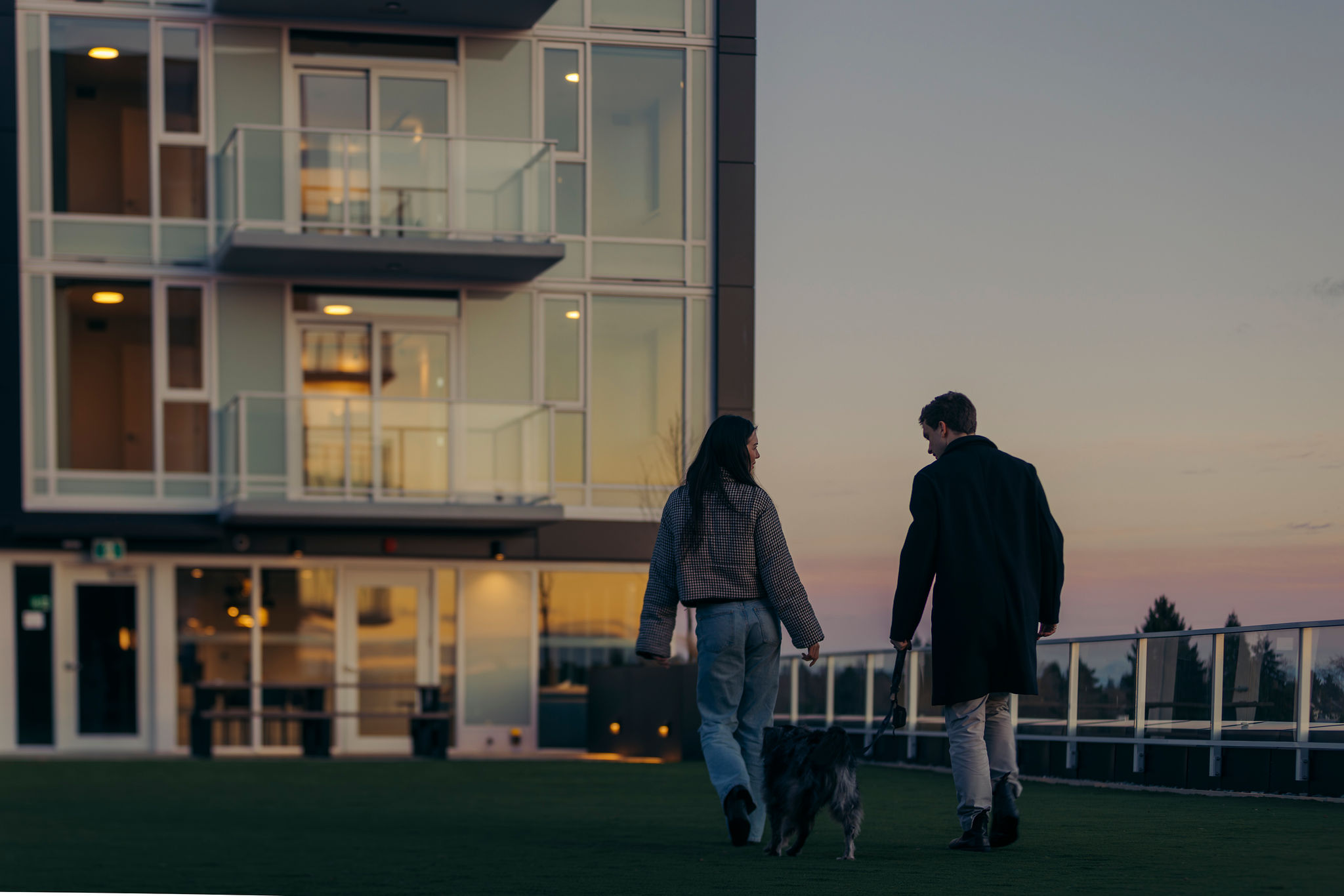 Residents walking a dog on rooftop terrace at modern concrete condo in East Vancouver at sunset