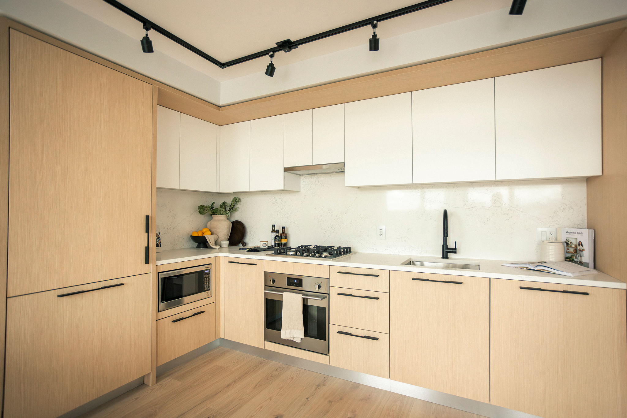 Modern L-shaped kitchen with light wood cabinetry, integrated appliances, and clean white backsplash in Vancouver condo